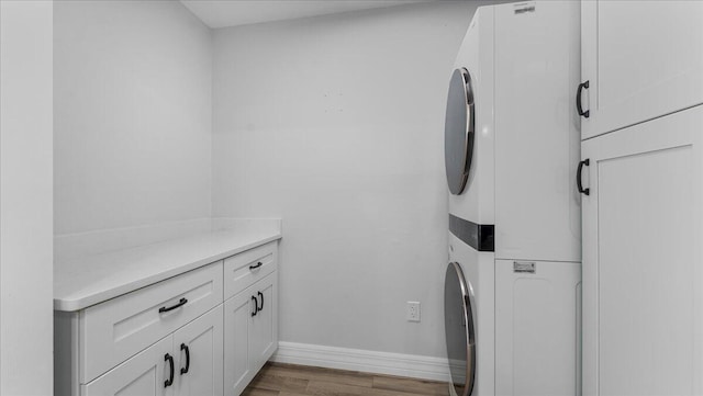 clothes washing area with light hardwood / wood-style flooring, cabinets, and stacked washer / dryer