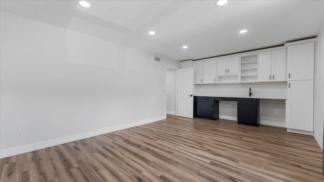 kitchen with white cabinetry, built in desk, and light wood-type flooring