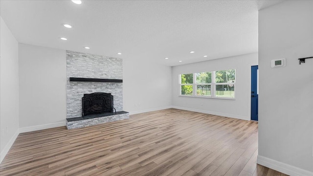 unfurnished living room with light wood-type flooring, a textured ceiling, and a fireplace