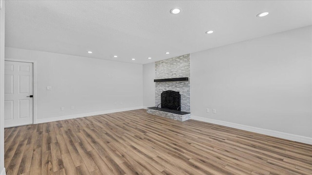 unfurnished living room featuring a stone fireplace, light hardwood / wood-style floors, and a textured ceiling