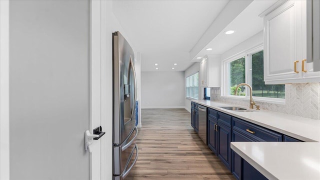 kitchen with blue cabinets, sink, white cabinetry, stainless steel appliances, and backsplash