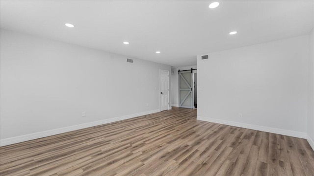 unfurnished room with a barn door and light wood-type flooring