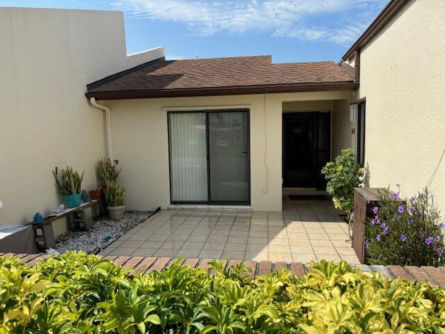 doorway to property featuring a patio area, roof with shingles, and stucco siding