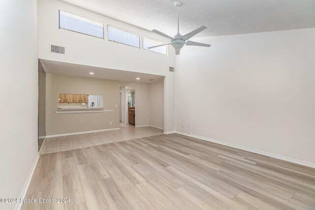 empty room featuring a high ceiling, ceiling fan, a textured ceiling, and light wood-type flooring