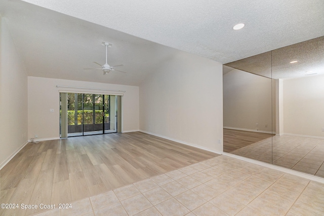 tiled empty room with ceiling fan, vaulted ceiling, and a textured ceiling