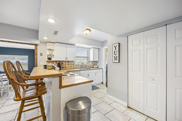 kitchen featuring white cabinetry, decorative backsplash, a kitchen breakfast bar, and kitchen peninsula