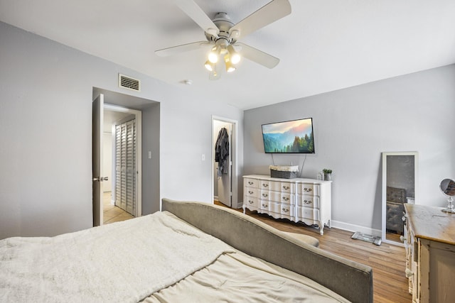 bedroom with a walk in closet, a closet, light wood-type flooring, and ceiling fan