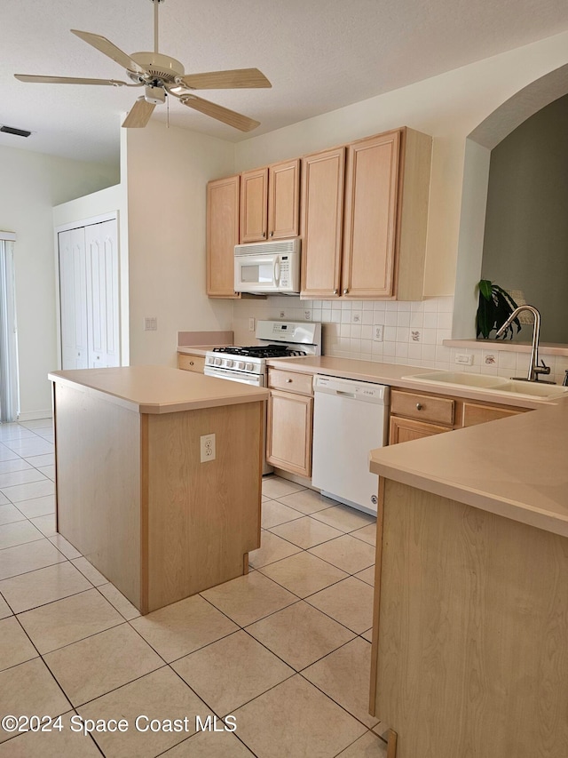 kitchen with light tile patterned floors, backsplash, light brown cabinetry, sink, and white appliances