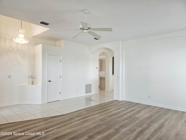 unfurnished room with ceiling fan with notable chandelier and light hardwood / wood-style floors