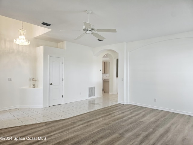empty room featuring arched walkways, visible vents, wood finished floors, and ceiling fan with notable chandelier