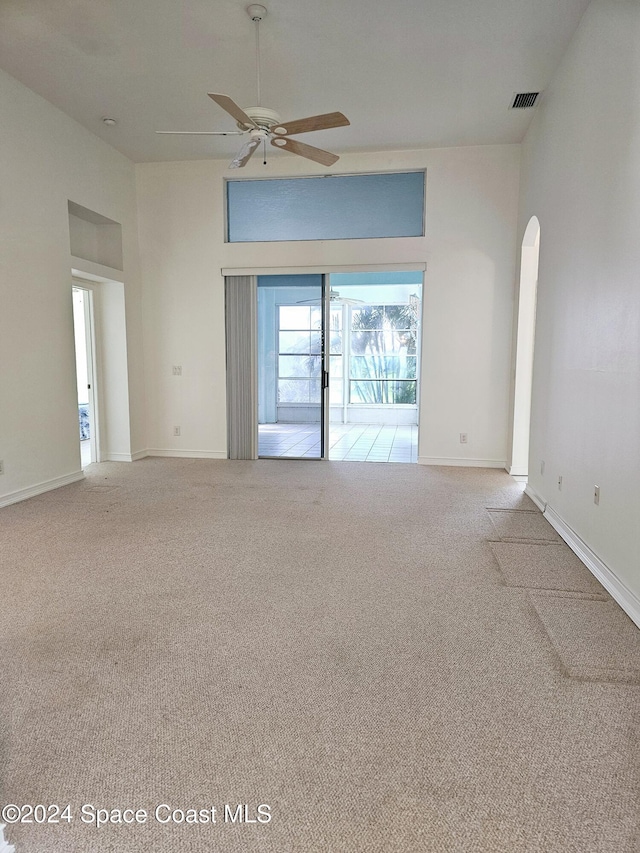 carpeted spare room featuring a ceiling fan, visible vents, baseboards, and arched walkways