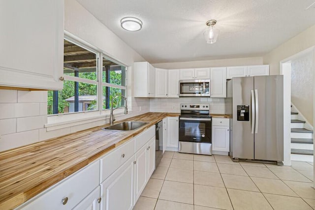 kitchen with stainless steel appliances, tasteful backsplash, wooden counters, white cabinets, and a sink