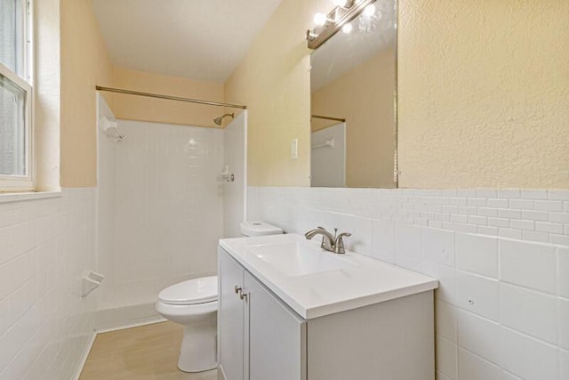 bathroom with a shower, tile walls, toilet, wainscoting, and vanity