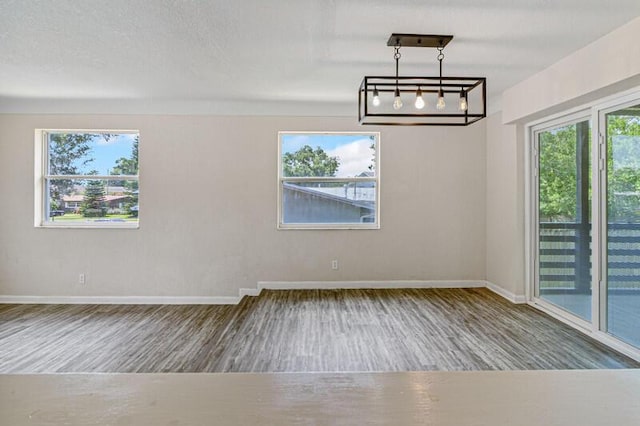 unfurnished dining area with a textured ceiling, baseboards, and wood finished floors