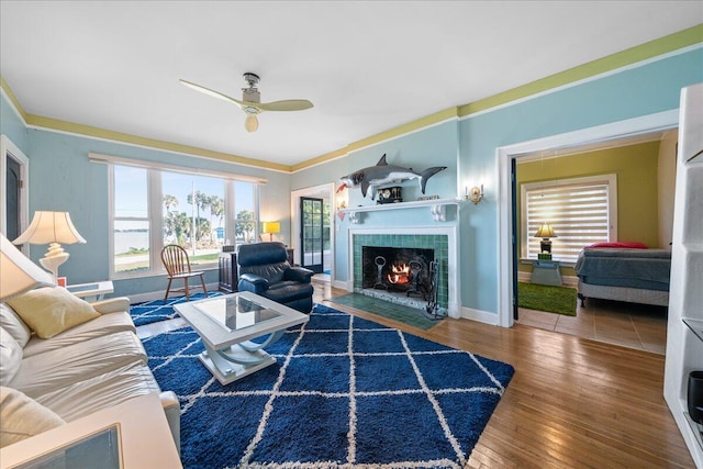 living room with hardwood / wood-style flooring, ceiling fan, ornamental molding, and a fireplace