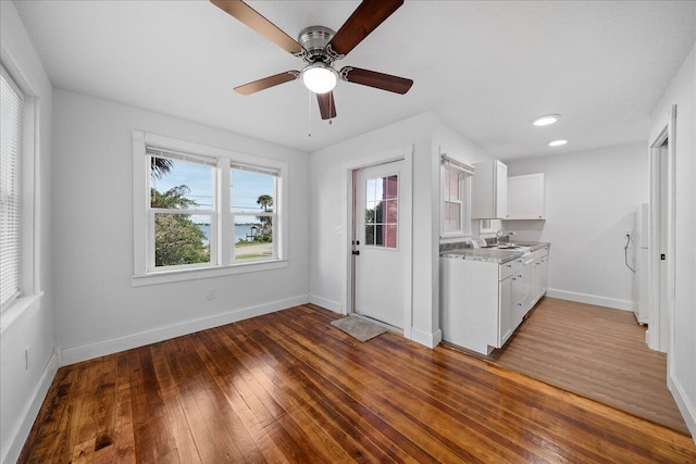 kitchen with sink, white cabinetry, light stone counters, wood-type flooring, and ceiling fan