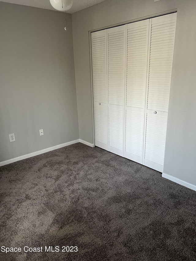 unfurnished bedroom with a textured ceiling, dark carpet, and a closet