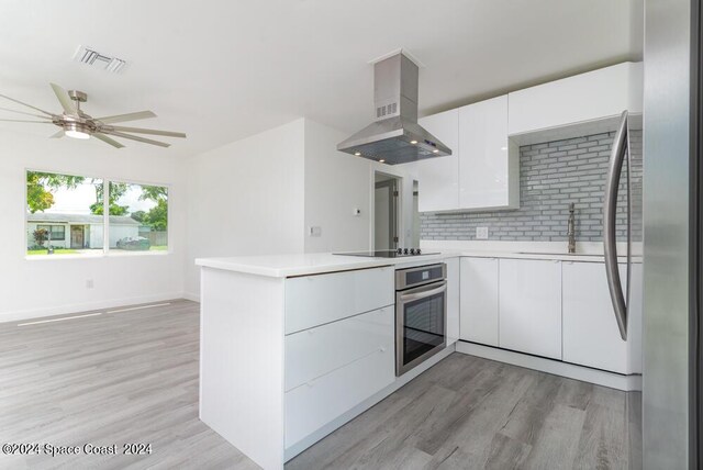 kitchen featuring sink, white cabinetry, stainless steel appliances, island range hood, and decorative backsplash