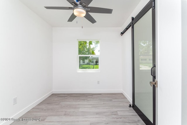 empty room with ceiling fan, a barn door, and light hardwood / wood-style floors