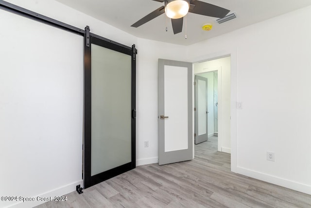 unfurnished bedroom with ceiling fan, a barn door, and light wood-type flooring