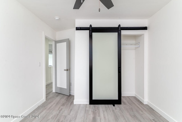 unfurnished bedroom featuring a closet, light hardwood / wood-style floors, a barn door, and ceiling fan