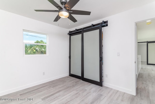 unfurnished bedroom with ceiling fan, a barn door, and light hardwood / wood-style flooring