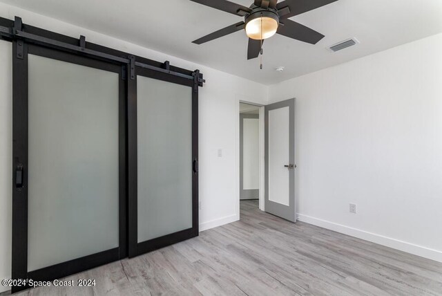 unfurnished bedroom featuring ceiling fan, a barn door, and light wood-type flooring