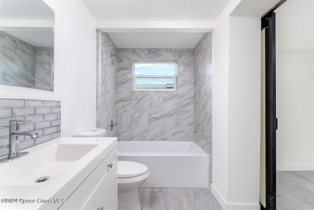 full bathroom with toilet, tiled shower / bath, wood-type flooring, vanity, and backsplash