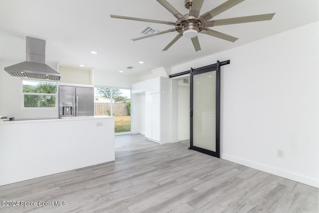 spare room featuring ceiling fan, a barn door, and light hardwood / wood-style floors