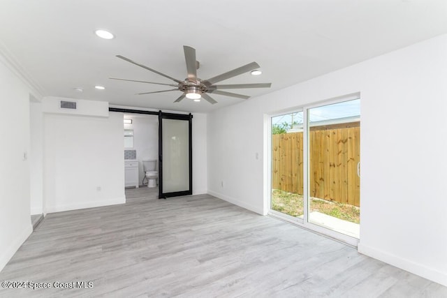 unfurnished room with light hardwood / wood-style flooring, a barn door, and ceiling fan