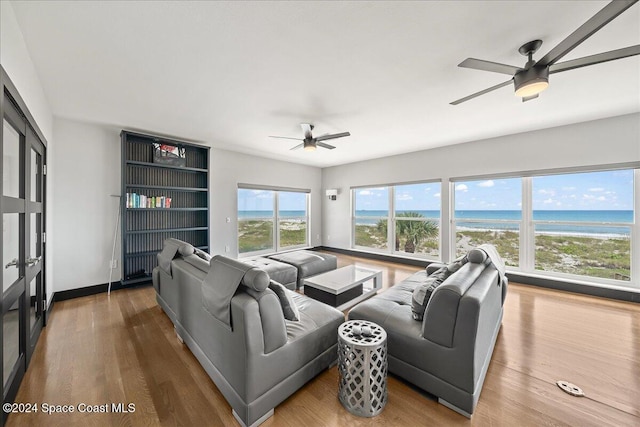 living room with ceiling fan, a water view, wood-type flooring, and a view of the beach