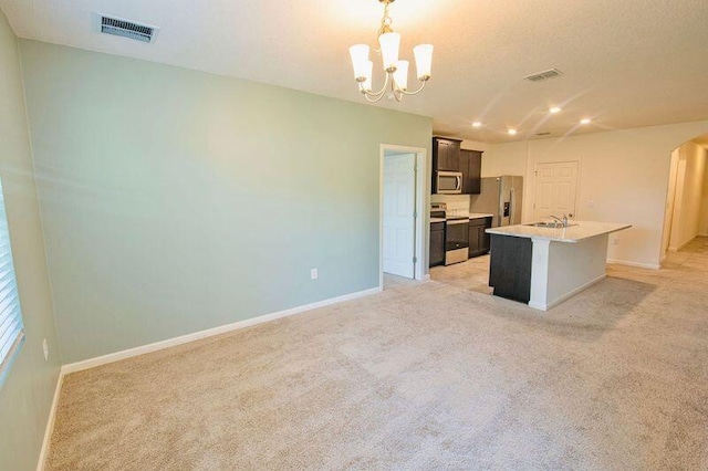 kitchen with sink, an inviting chandelier, hanging light fixtures, an island with sink, and stainless steel appliances