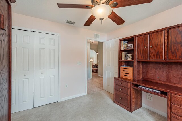 unfurnished office featuring ceiling fan, built in desk, and light colored carpet