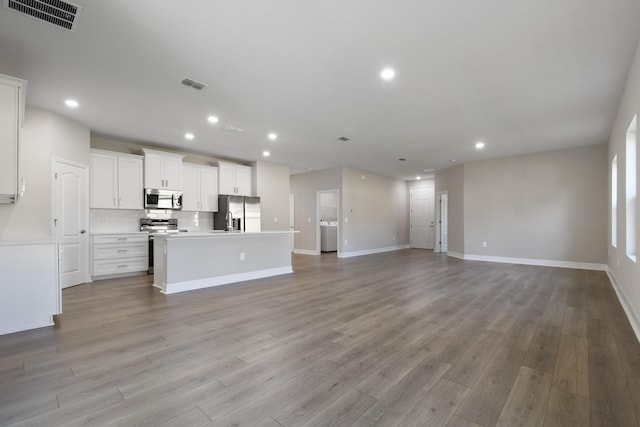 kitchen with appliances with stainless steel finishes, white cabinetry, a kitchen island with sink, decorative backsplash, and light wood-type flooring