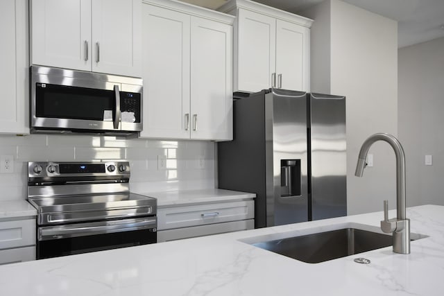 kitchen with sink, white cabinetry, light stone counters, stainless steel appliances, and decorative backsplash