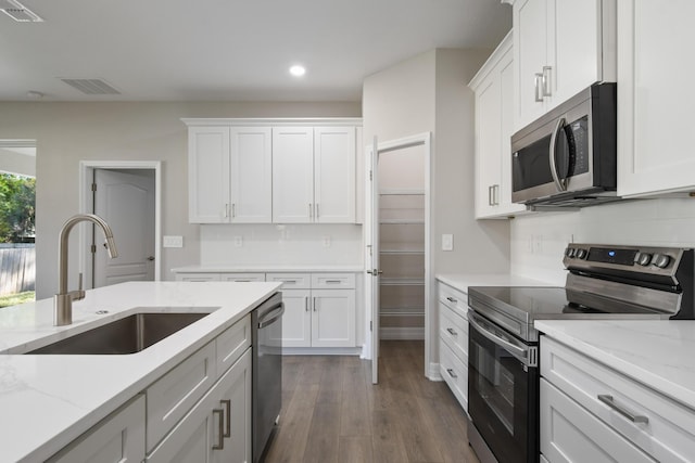 kitchen with stainless steel appliances, white cabinetry, light stone countertops, and sink