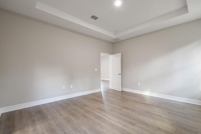 spare room with a tray ceiling and light hardwood / wood-style flooring