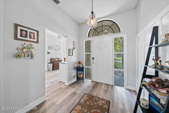 foyer with a towering ceiling, a textured ceiling, and light hardwood / wood-style flooring