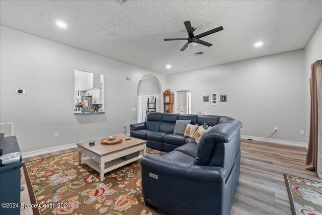 living room featuring ceiling fan, light wood-type flooring, and a textured ceiling