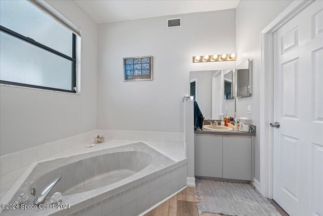 bathroom with hardwood / wood-style floors, vanity, and tiled tub