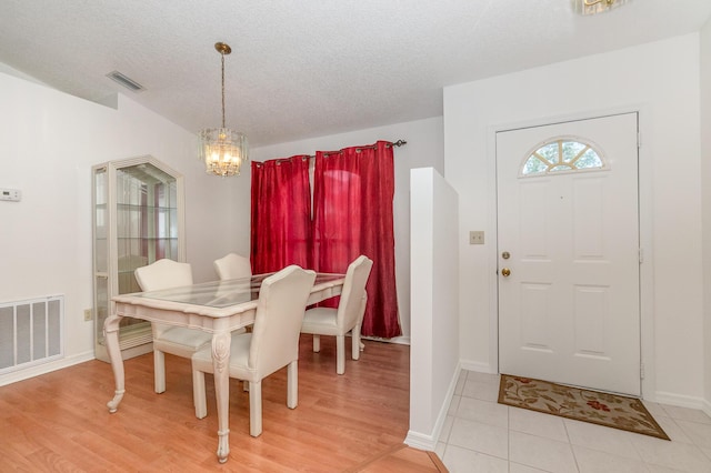 dining space with an inviting chandelier, light hardwood / wood-style floors, and a textured ceiling