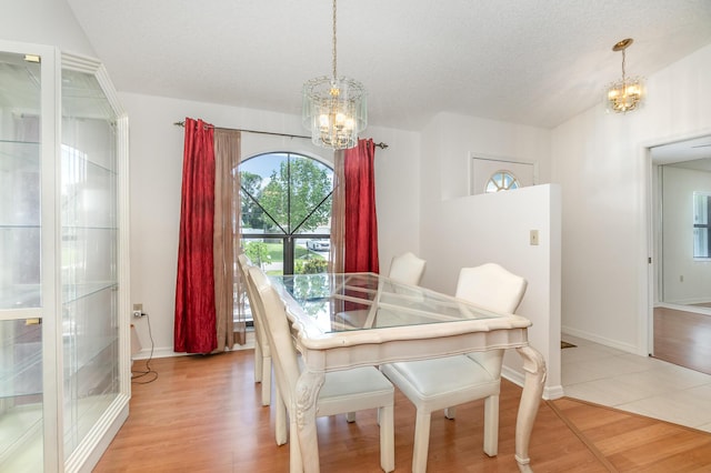 dining area featuring an inviting chandelier, lofted ceiling, a textured ceiling, and light wood-type flooring