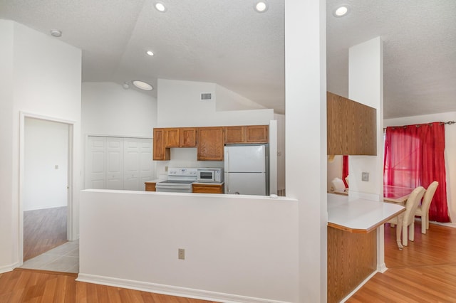 kitchen with light hardwood / wood-style floors, a textured ceiling, white appliances, and kitchen peninsula