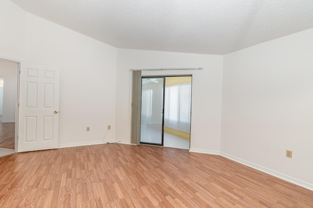 spare room featuring vaulted ceiling, a textured ceiling, and light hardwood / wood-style flooring