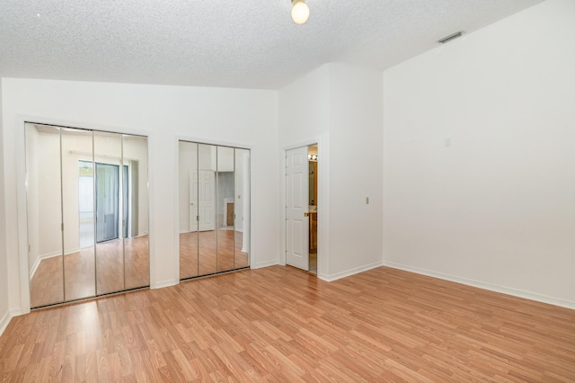 unfurnished bedroom featuring a textured ceiling, light hardwood / wood-style flooring, multiple closets, and vaulted ceiling