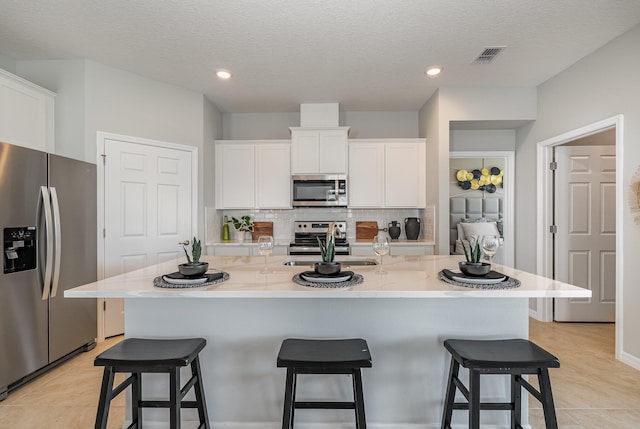 kitchen featuring a kitchen bar, a center island with sink, white cabinets, and appliances with stainless steel finishes