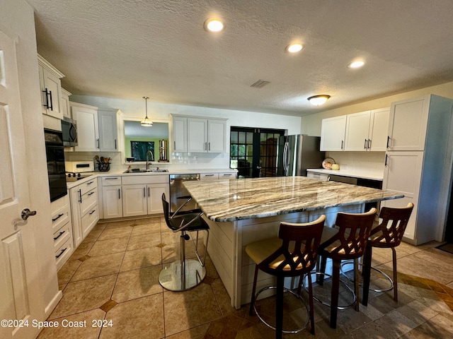 kitchen with appliances with stainless steel finishes, hanging light fixtures, a kitchen island, a breakfast bar area, and sink