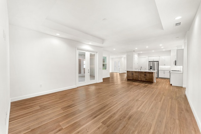 unfurnished living room featuring light hardwood / wood-style flooring, sink, and french doors