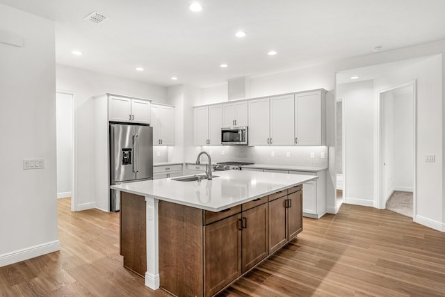 kitchen featuring decorative backsplash, an island with sink, light wood-type flooring, sink, and appliances with stainless steel finishes