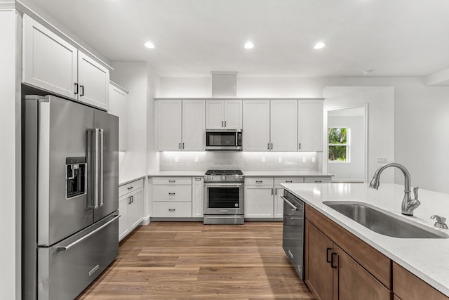 kitchen with sink, white cabinetry, hardwood / wood-style flooring, and high end appliances